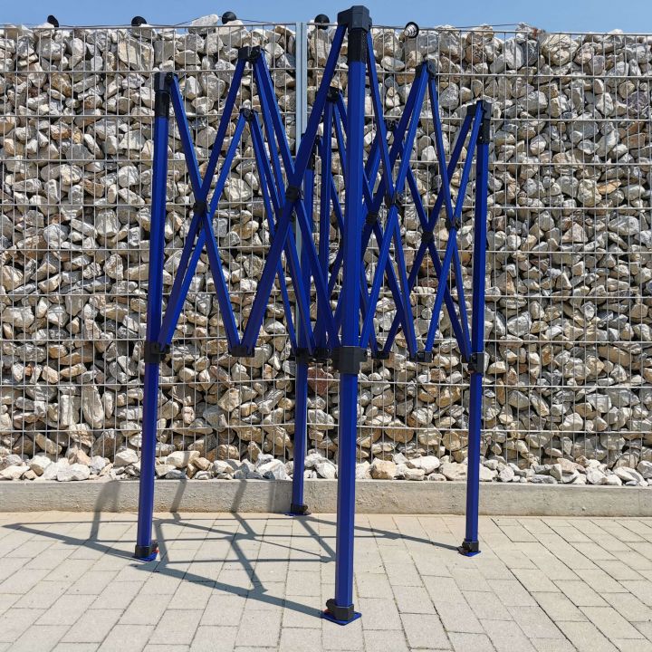 Collapsed but unshot blue frame of the scissor party tent, standing on the pavement with pebbles in the background (by the fence).