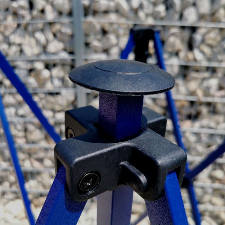 Detail of the black roof/top connecting part and plastic sliding mechanism on the blue structure of the tent, with a gravel background.