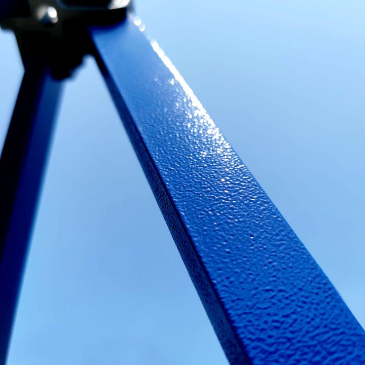 Detail of the blue metal pole/leg of the tent with a finely textured surface (probably powder-coated) against the blue sky.