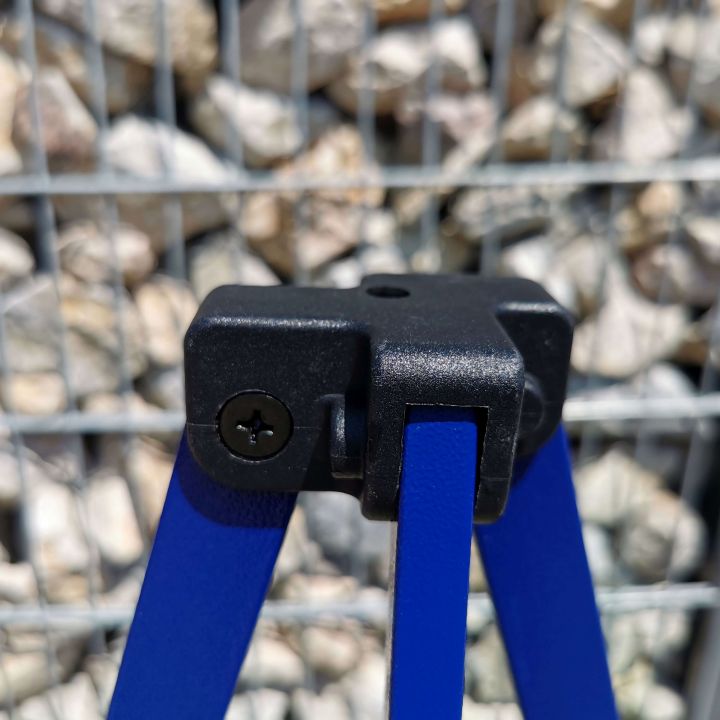 Detail of the black plastic connecting part (top part of the leg) on the blue tent structure, with a background made of gray pebbles/gravel.